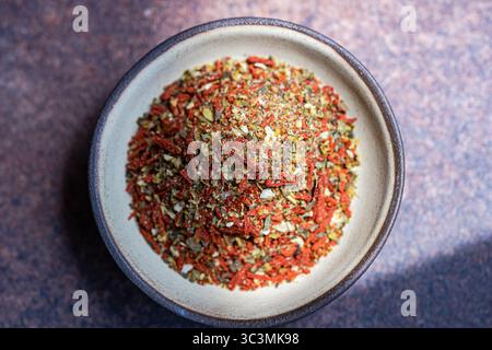Top view of a vibrant spice blend containing tomato and olive, seasoned with salt, displayed in a beige ceramic bowl against a textured stone brown ba Stock Photo