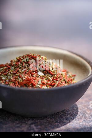 A close-up of a bowl filled with a vibrant mix of dried tomatoes and spices, accented by olive and salt. The rustic black ceramic bowl sits on a textu Stock Photo