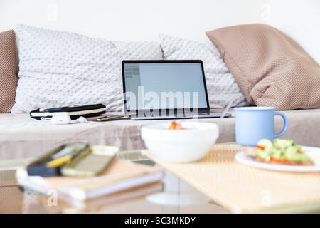 A cozy workspace setup featuring a laptop on a couch, surrounded by pillows and a table with a fresh meal and coffee, creating a peaceful and producti Stock Photo