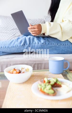 A Latin woman relaxes at home with a laptop, enjoying small everyday life moments with a cozy atmosphere around her, reflecting a sense of comfort and Stock Photo