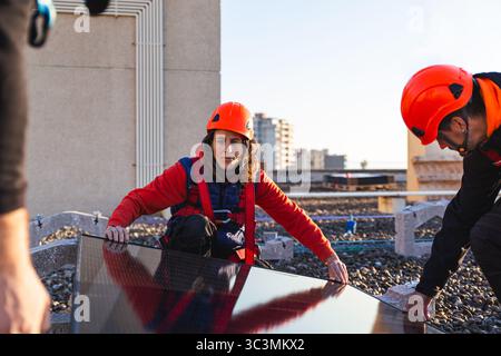 Engineers wearing safety gear work on installing solar panels on a rooftop. The image highlights sustainable energy efforts through solar technology, Stock Photo