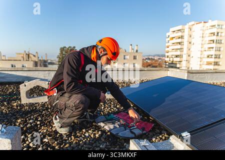 A technician on a city rooftop is installing solar panels, using tools from an open toolkit. The image showcases renewable energy efforts in an urban Stock Photo