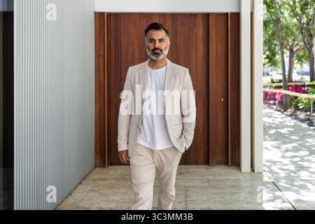 An Indian man casually strolls with confidence in a light summer suit and a white t-shirt. The relaxed attire and vibrant backdrop suggest a carefree Stock Photo