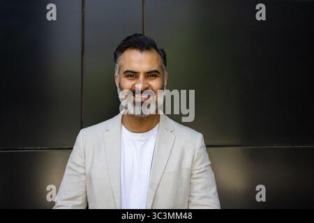 Confident Indian man in a light summer blazer, smiling warmly against a dark backdrop. Perfect image symbolizing travel, summer, and multicultural exp Stock Photo