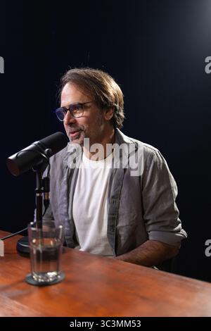 A professional podcast recording studio featuring a man speaking into a microphone, wearing casual attire, and surrounded by studio equipment, emphasi Stock Photo