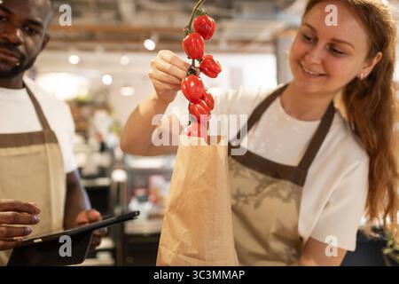 A man and woman work together in an eco-friendly store, packing fresh tomatoes into a paper bag. The ambiance highlights sustainability and teamwork i Stock Photo