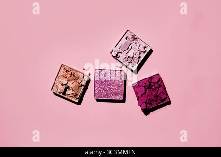 Top view of four vibrant, broken eyeshadow squares on a soft pink background. The colors include pink, purple, mauve, and bronze, showcasing a creativ Stock Photo