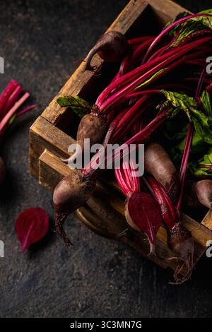 Top view of fresh, organic beetroots with vivid red stems and lush green leaves in a wooden crate on a dark background, showcasing their natural textu Stock Photo