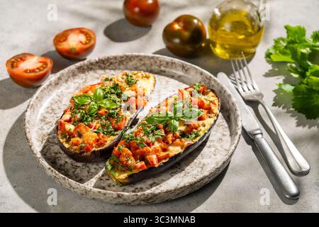 Delicious stuffed baked eggplant garnished with fresh vegetables, herbs, and spices. Served on a rustic plate, offering a healthy and flavorful vegeta Stock Photo
