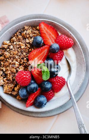 A delicious bowl of granola topped with fresh red berries, including strawberries, raspberries, and blueberries, accompanied by creamy yogurt for a nu Stock Photo
