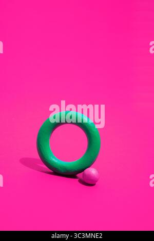 A vibrant image featuring a green ring shape and a magenta sphere set against a bright magenta background, creating a striking visual contrast with ge Stock Photo