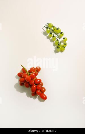 Top view of playful fruits with cherry tomatoes styled as grape clusters and grapes posing as cherry tomatoes on a white background, bringing fun to f Stock Photo