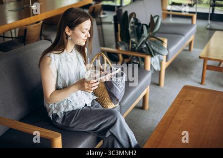 A woman enjoys a moment of relaxation with her coffee in a stylish cafe. Seated comfortably, she seems content and engaged, highlighting a peaceful am Stock Photo