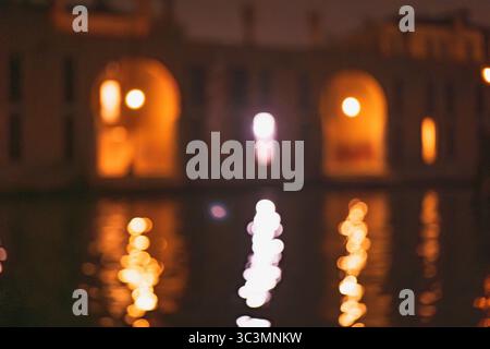 Blurred warm lights reflect on water, creating a mystical and abstract scene. The orange and white hues evoke a sense of magic and depth, enhancing th Stock Photo