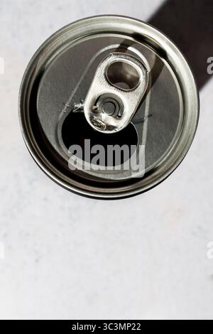 Top view of an open soda can with a pull-tab lid, casting a shadow on a light gray, textured background. The aluminum can gleams under soft studio lig Stock Photo