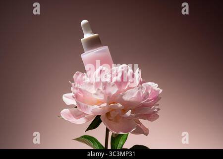 A pink cosmetic dropper bottle elegantly rests atop a blooming peony, set against a soft, muted background. The image embodies luxury, beauty, and nat Stock Photo