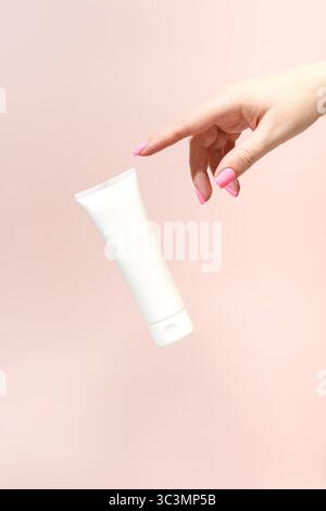 A woman's hand with pink nails, delicately decorated with a white cosmetic tube on a soft pink background, gives a fresh, summery look. Ideal for beau Stock Photo