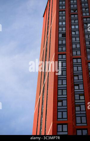 A modern urban skyscraper with a striking red facade stands tall against a clear blue sky. The building's sleek design and numerous windows reflect co Stock Photo