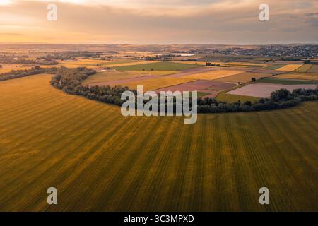 Aerial view of expansive fields in Ontigola, Toledo, Spain, during the golden hour, highlighting diverse agricultural plots bordered by lush trees und Stock Photo