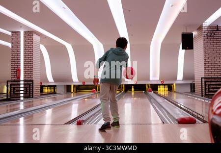 A boy enjoying a game of bowling in a modern alley with bright lighting. He is focused on rolling the ball towards the pins, showcasing skill and conc Stock Photo
