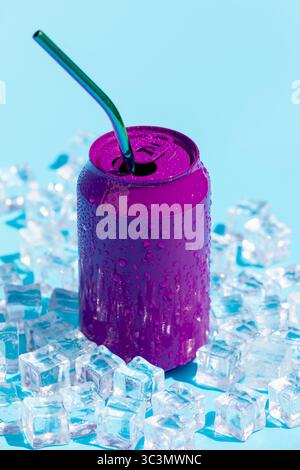 A vibrant purple soda can with a straw amidst scattered ice cubes. The droplets on the can emphasize its refreshing nature, set against a bright blue Stock Photo