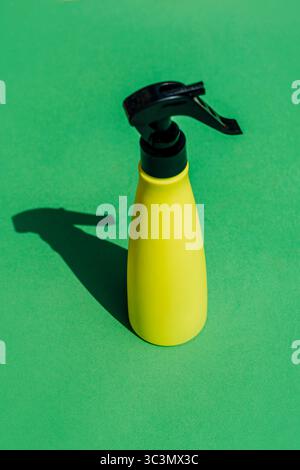 Top view studio shot of a yellow spray bottle on a green background. The sleek design of the bottle against the vibrant backdrop emphasizes a minimali Stock Photo
