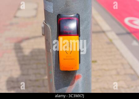 Close-up view of a pedestrian traffic signal button on a metal pole, featuring warning lights and instructions in German, set against a city street ba Stock Photo