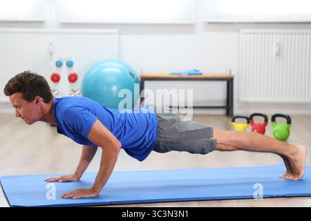 young man, blue shirt on fitness mat doing push-ups Stock Photo
