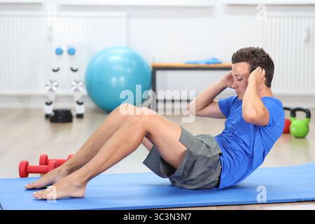 young man, blue shirt barefoot on fitness mat doing sit ups Stock Photo