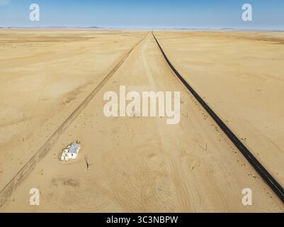 Aerial view of a solitary road cutting through the vast, undulating ochre dunes under a pale sky, a stark contrast, Walvis Bay Lagoon, Walvis Bay, Namibia. Stock Photo