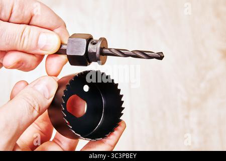 Mandrel with pilot drill bit held in one hand hole saw with teeth held in other hand unassembled woodcutting tool components visible from side angle. Stock Photo