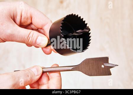 Spade bit and hole saw drill bit for woodworking held in hands close to each other ready to be attached to cordless drill for woodwork tasks. Stock Photo