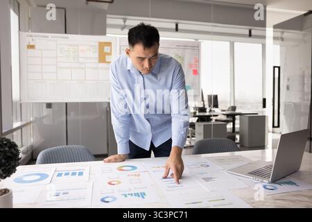 Focused Chinese professional man reviewing printed charts and graphs Stock Photo