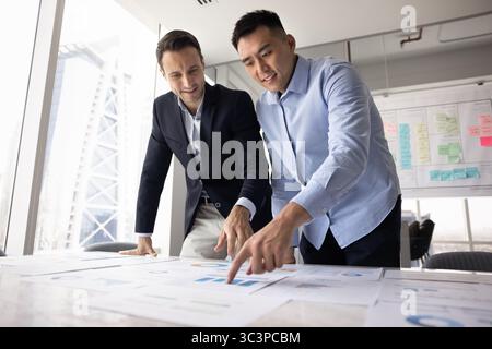 Two diverse teammates analyzing printed graphs and charts Stock Photo