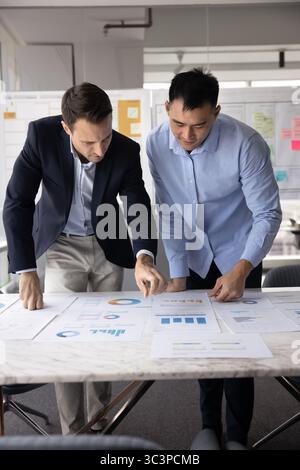 Colleagues deeply engaged in analyzing printed financial and statistical charts Stock Photo