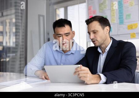 Two professional men looking at tablet screen seated at table Stock Photo
