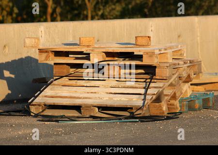 Multiple old wooden pallets are stacked haphazardly on asphalt, showing surface wear and some warping, illustrating common materials handling Stock Photo