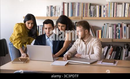 Multiethnic professionals gathered around laptop, collaborating on project or presentation Stock Photo