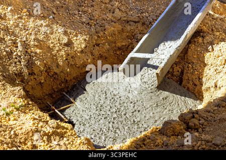 Workers pour fresh concrete into trench at construction site, ensuring solid foundations for new structure. Stock Photo