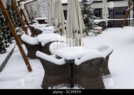 Closed outdoor cafe during winter. Tables and chairs of an outdoor cafe covered in snow. Stock Photo