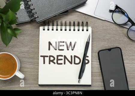 New Trends inscription in notebook, coffee, laptop, smartphone and pen on wooden table, top view Stock Photo