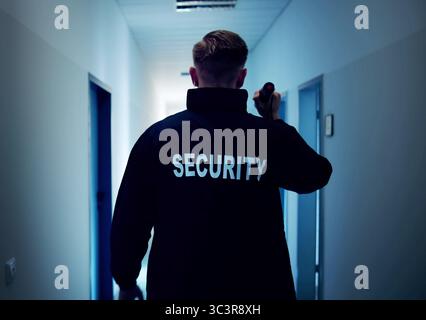 Night Security Guard Patrolling Warehouse In Uniform With Flashlight, Ensuring Safety. Stock Photo