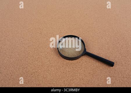 Magnifying glass placed on a cork board background. Idea for searching, detective work or typing text Stock Photo
