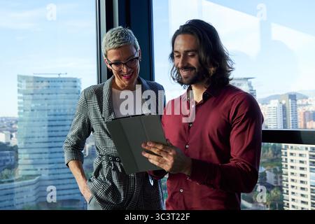 Businesspeople using tablet, working together in modern office with city view. Stock Photo
