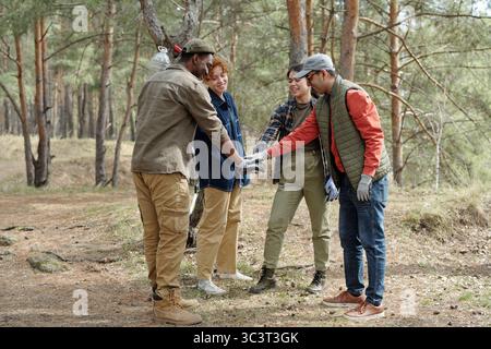 Diverse Young Adults Gathering Outdoors and Stacking Hands in Forest Stock Photo