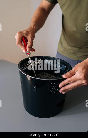 Vertical cropped shot of unrecognizable man using screwdriver to repair air humidifier, emphasizing importance of regular maintenance for optimal Stock Photo