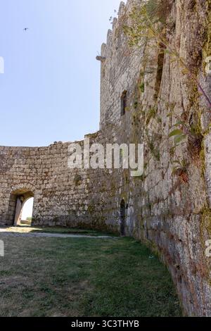 A stone wall with a small archway in the middle. The wall is covered in moss and the archway is open Stock Photo