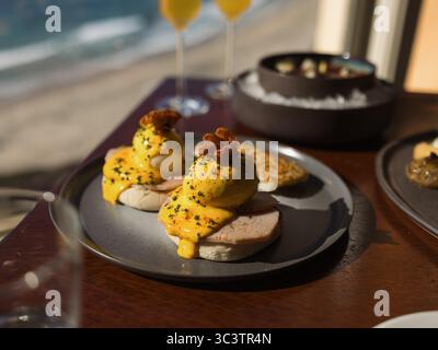 Gourmet eggs Benedict with creamy hollandaise sauce and poached eggs. Elegant brunch dish with bacon on toasted English muffins at upscale cafe. Stock Photo