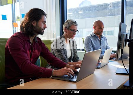 Three multiracial business colleagues sitting in the office working using laptops. Stock Photo