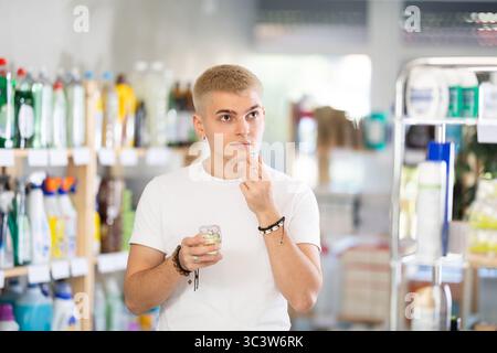 Happy young guy emotionally choosing perfume in cosmetics store Stock Photo